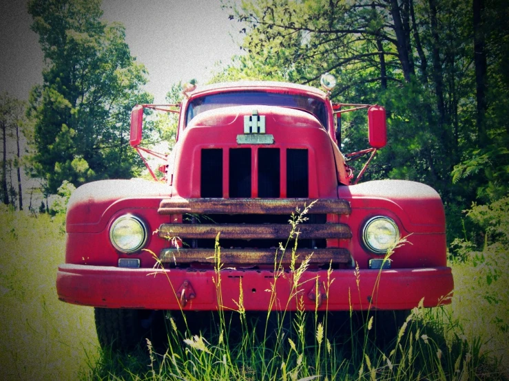 an old red truck sitting in a field