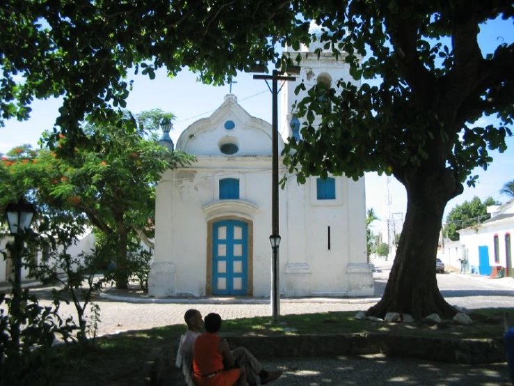 two people sit on a bench near the street near a church