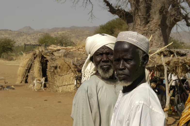 two black people stand near the huts in a remote area