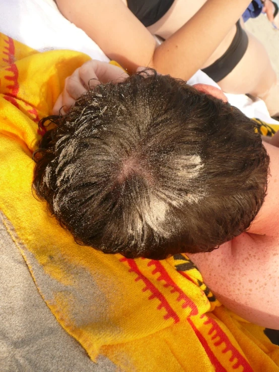 a man laying down on top of a towel near someone