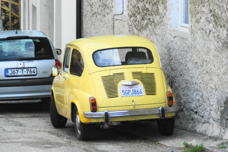 small yellow, old style car parked next to two older cars