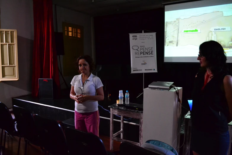 two women standing next to each other in front of a projection screen