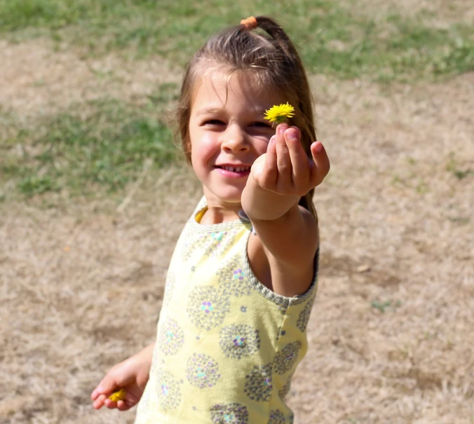 a smiling child with a yellow flower in her hand