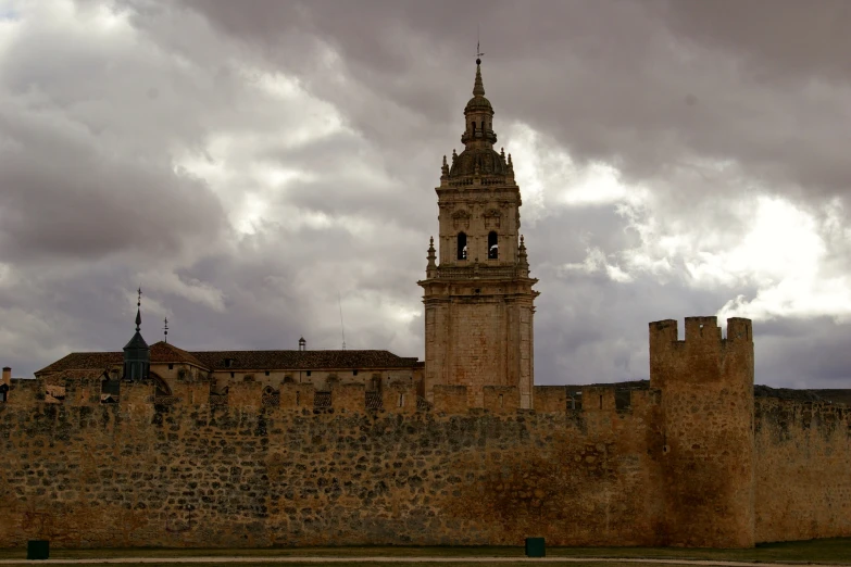 old brick wall with bell tower against cloudy sky