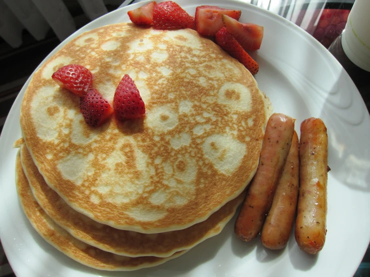 pancakes topped with strawberries and sausages on a white plate