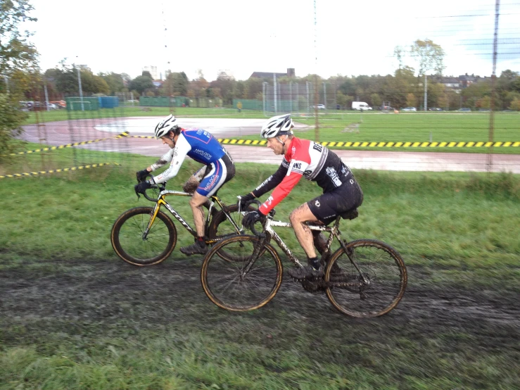 two people racing bikes down the middle of a field