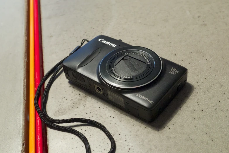 a black digital camera sitting on a table with a rainbow pencil nearby