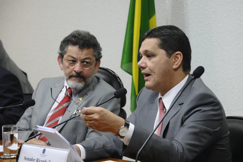 a meeting with three men sitting and a microphone