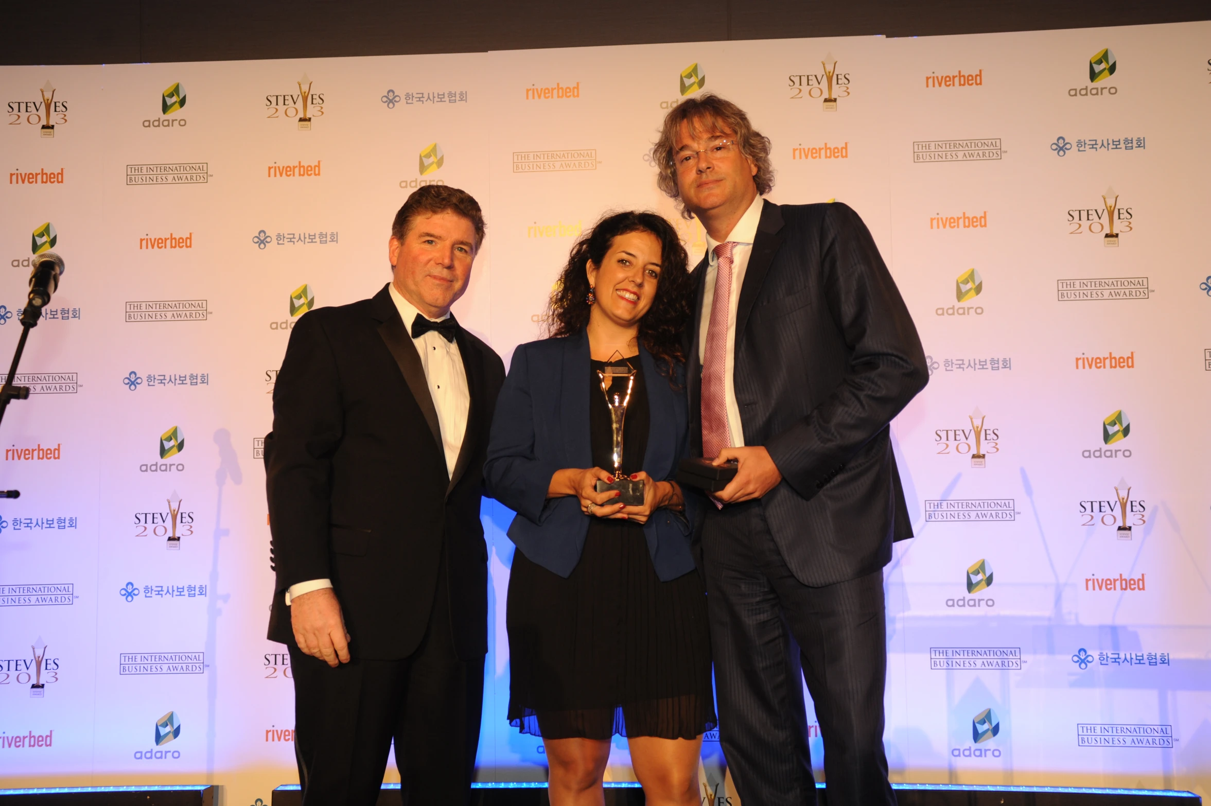 three men in suits posing together with one holding a trophy