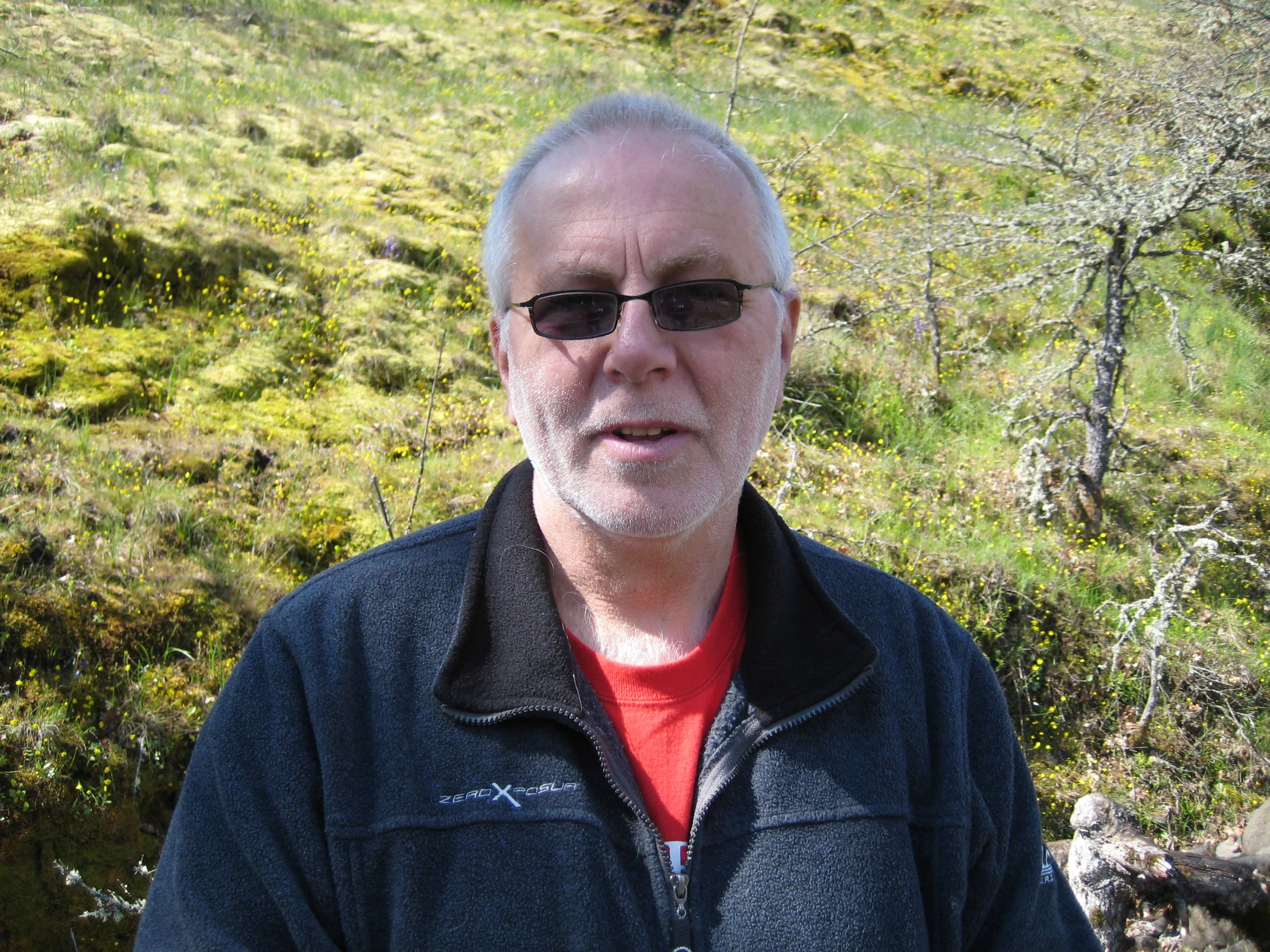 an older man wearing shades standing in the grass