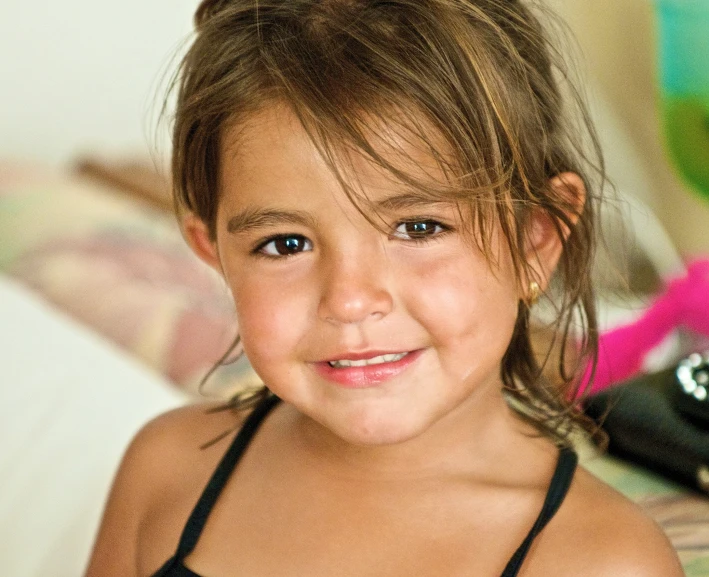 a little girl smiles while sitting on her bed