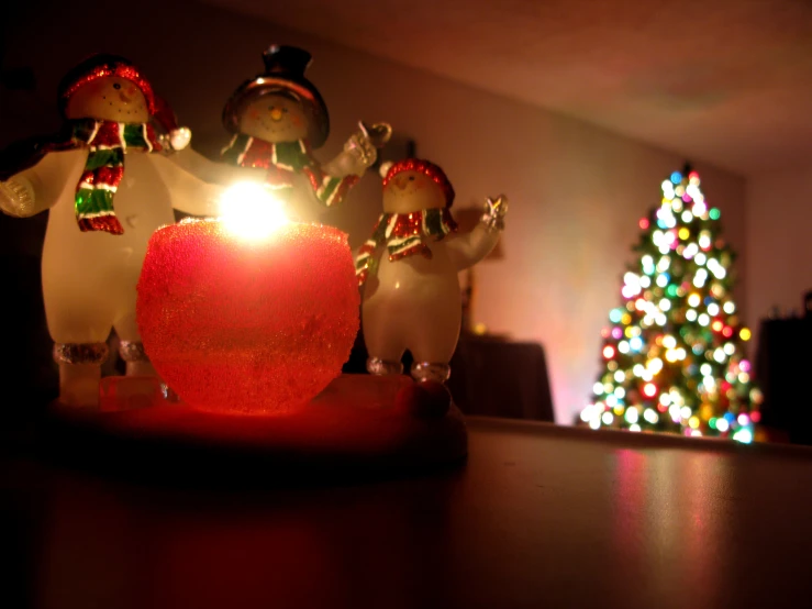 two small ornaments sit by a lighted candle on a table