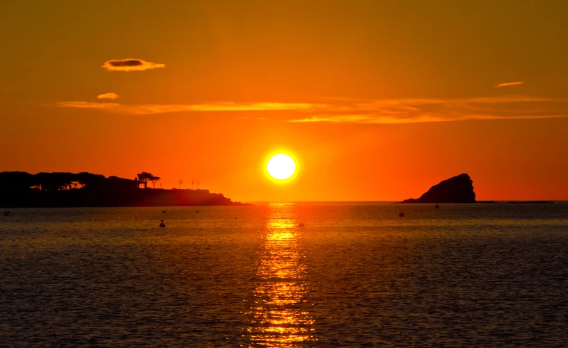 a sunset over the ocean with some hills in the background