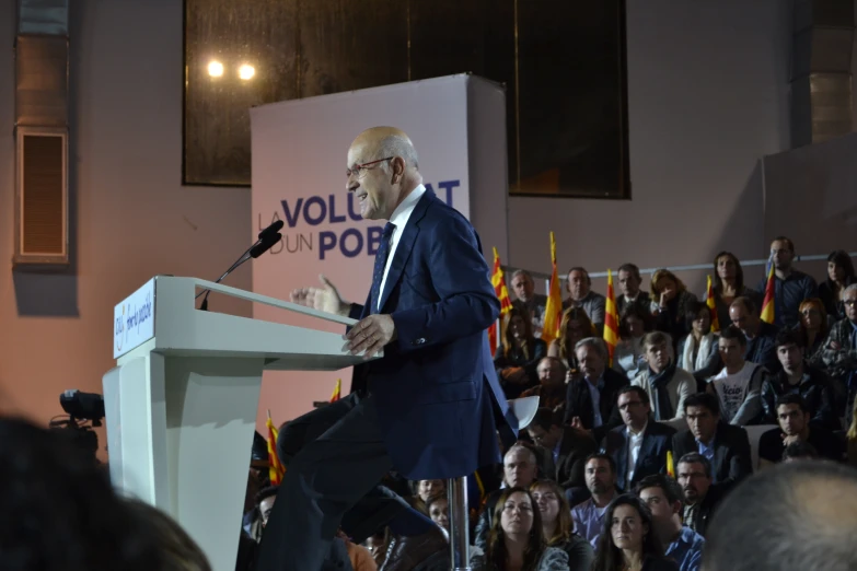 man speaking into microphone at podium at podium in front of large audience