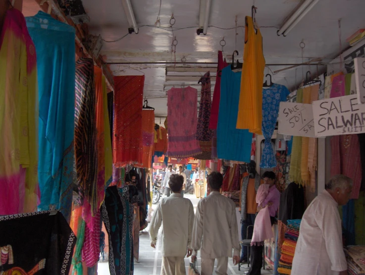 people walk down the sidewalk past a store filled with sale scarves