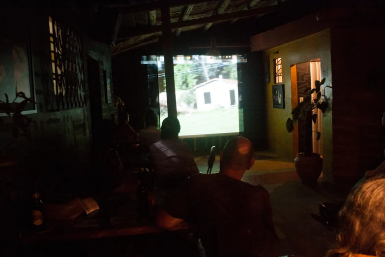 people sitting down watching a projector screen outside of a home