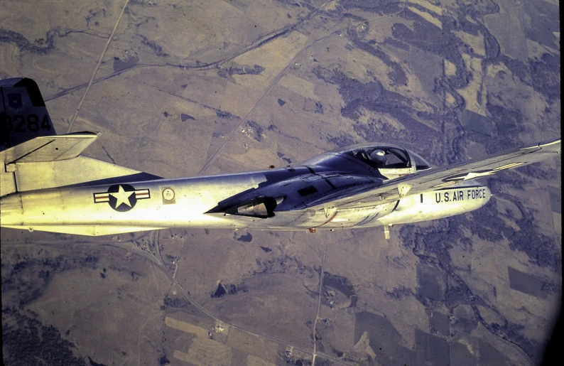 a fighter jet flying over the ground near a mountainous area