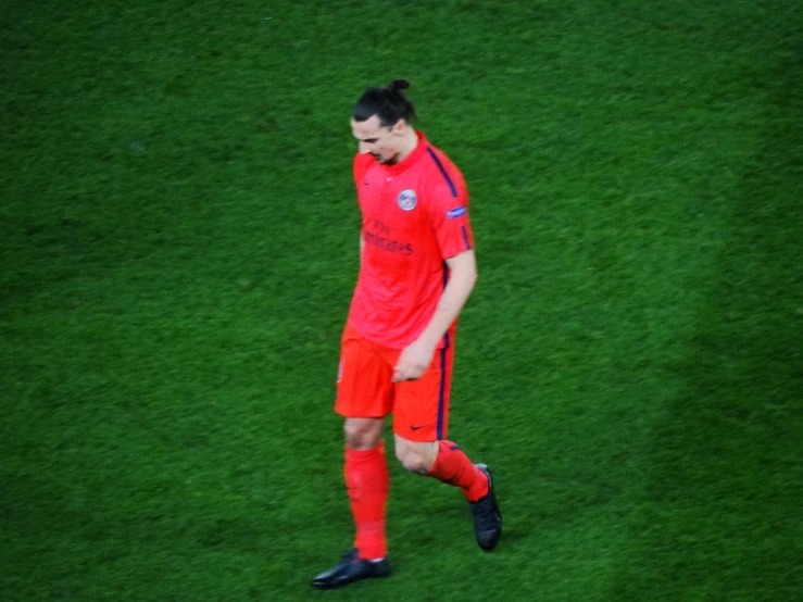 a person in orange stands on grass near a soccer ball