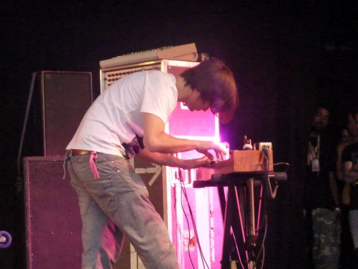 a guy in jeans and a white shirt at a keyboard on stage