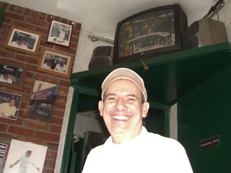 a man in a hat smiling next to a shelf with pictures