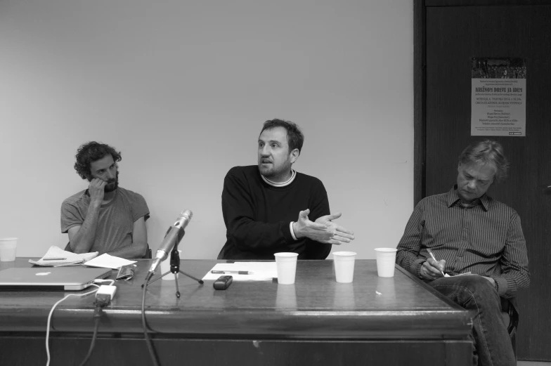 three men in a discussion sitting at a long table