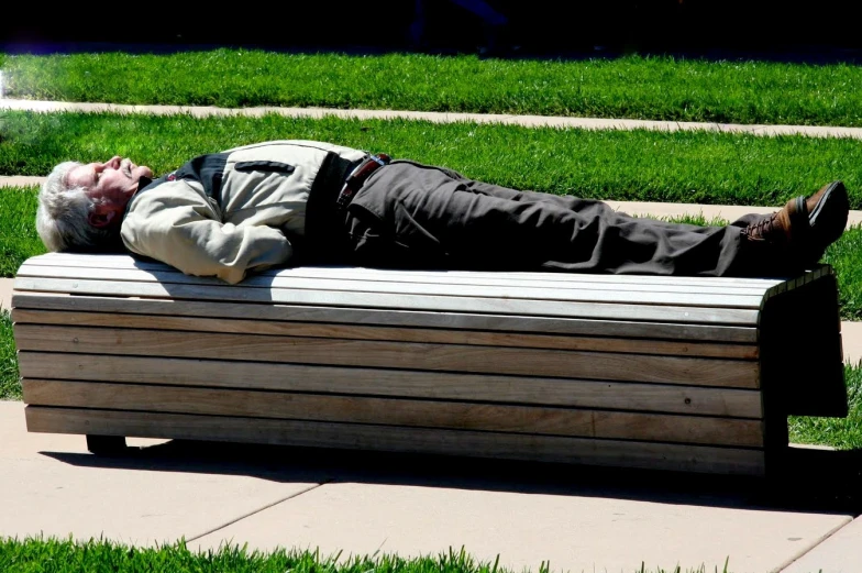 a man sleeping on a wooden bench next to a park