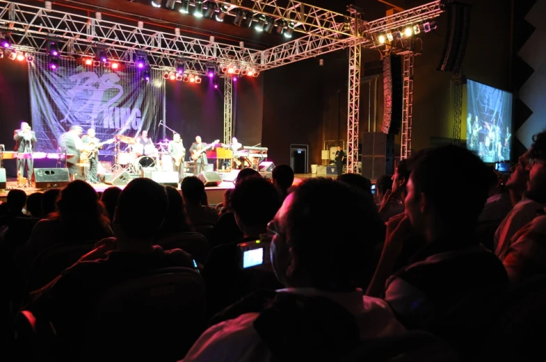 a crowd watches a concert being projected on an outdoor screen