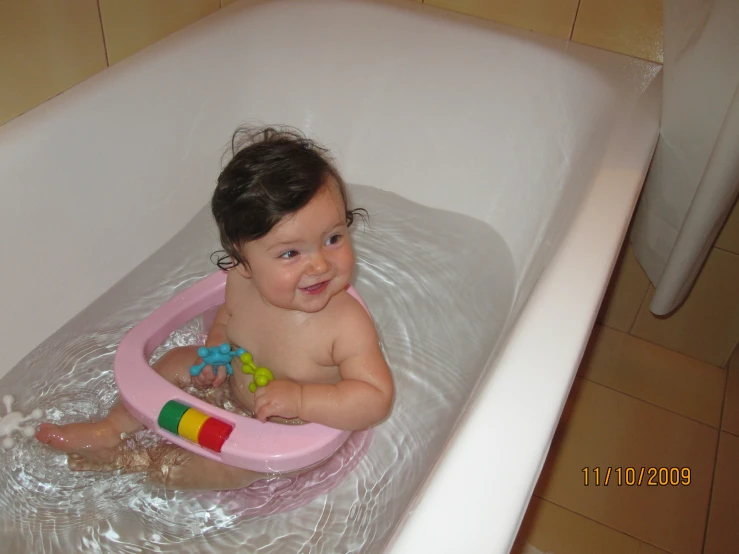 the little baby smiles while sitting in a bathtub