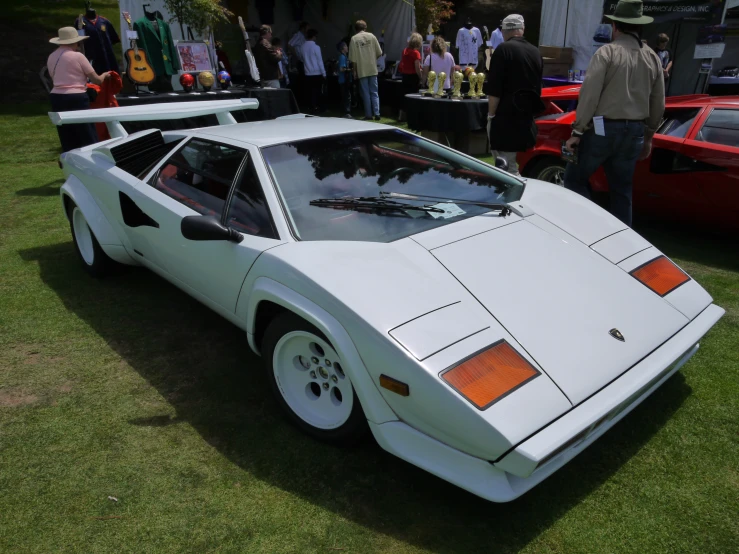 a white sports car parked in the grass near some other vehicles