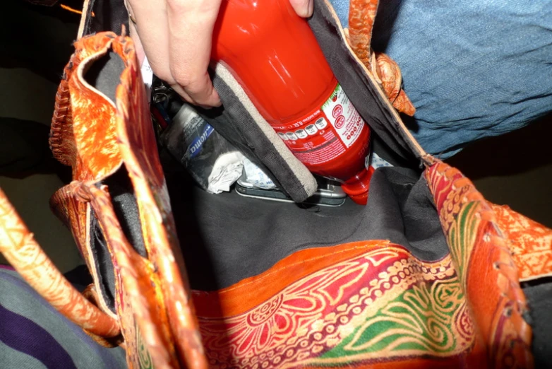 someone has their hand in the pocket of a purse with a red bottle