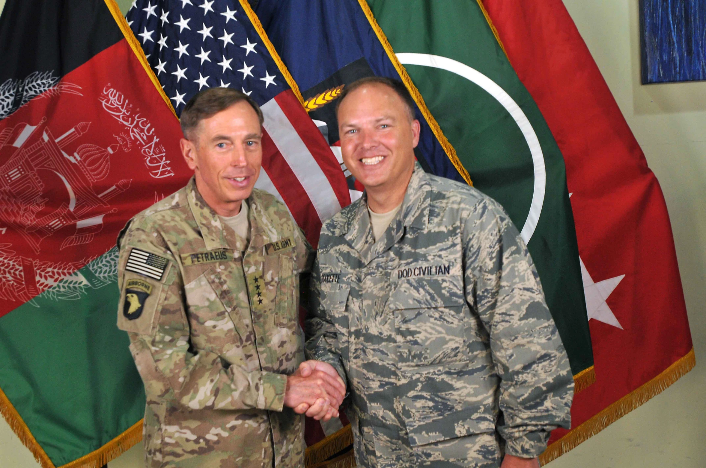 two people shake hands in front of flags