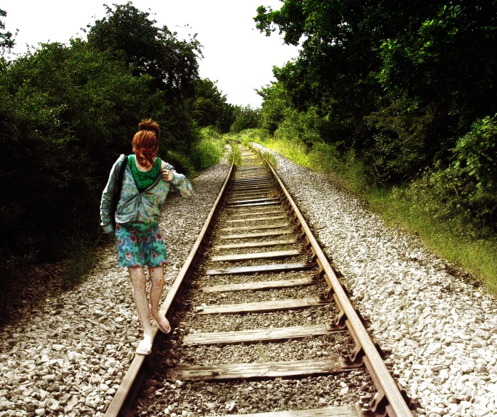 a woman walking up the middle of railroad tracks