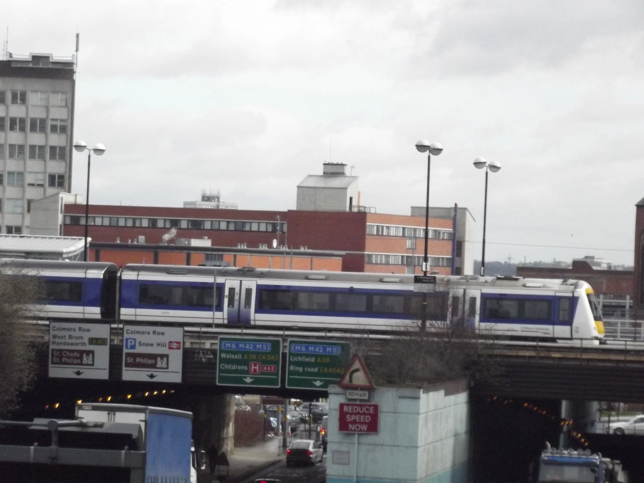 a very busy city area with traffic and a train going over the bridge