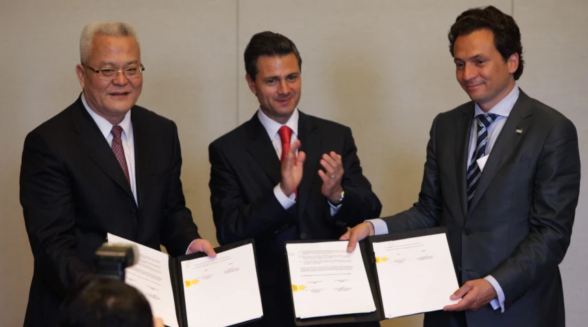 three men in suits are holding papers and smiling