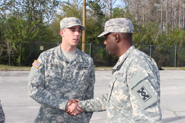 three men in camouflage uniforms shake hands in the middle of an empty parking lot