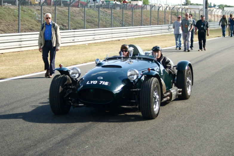 vintage race car being followed by men on a race track