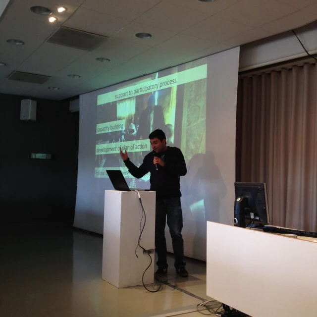 a man speaking at a podium in front of a screen