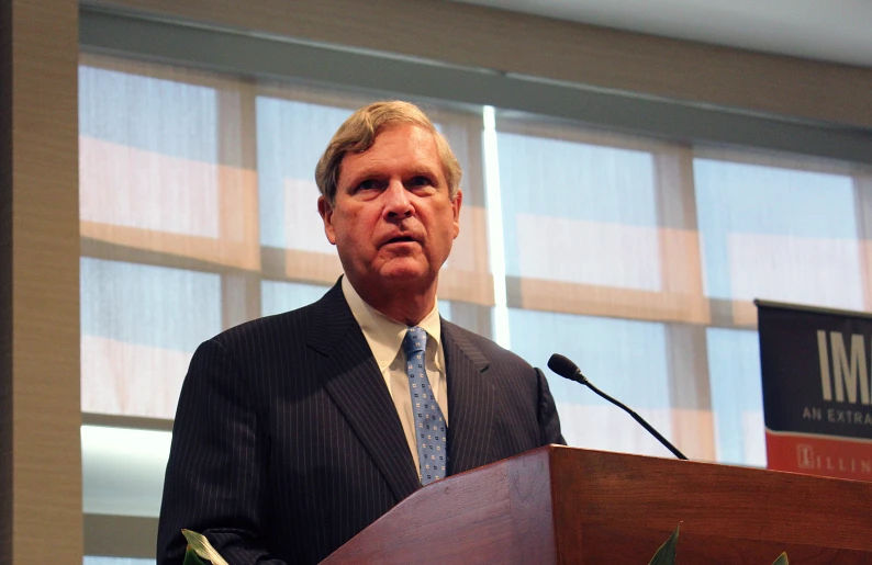 an older man standing at a podium in front of a microphone