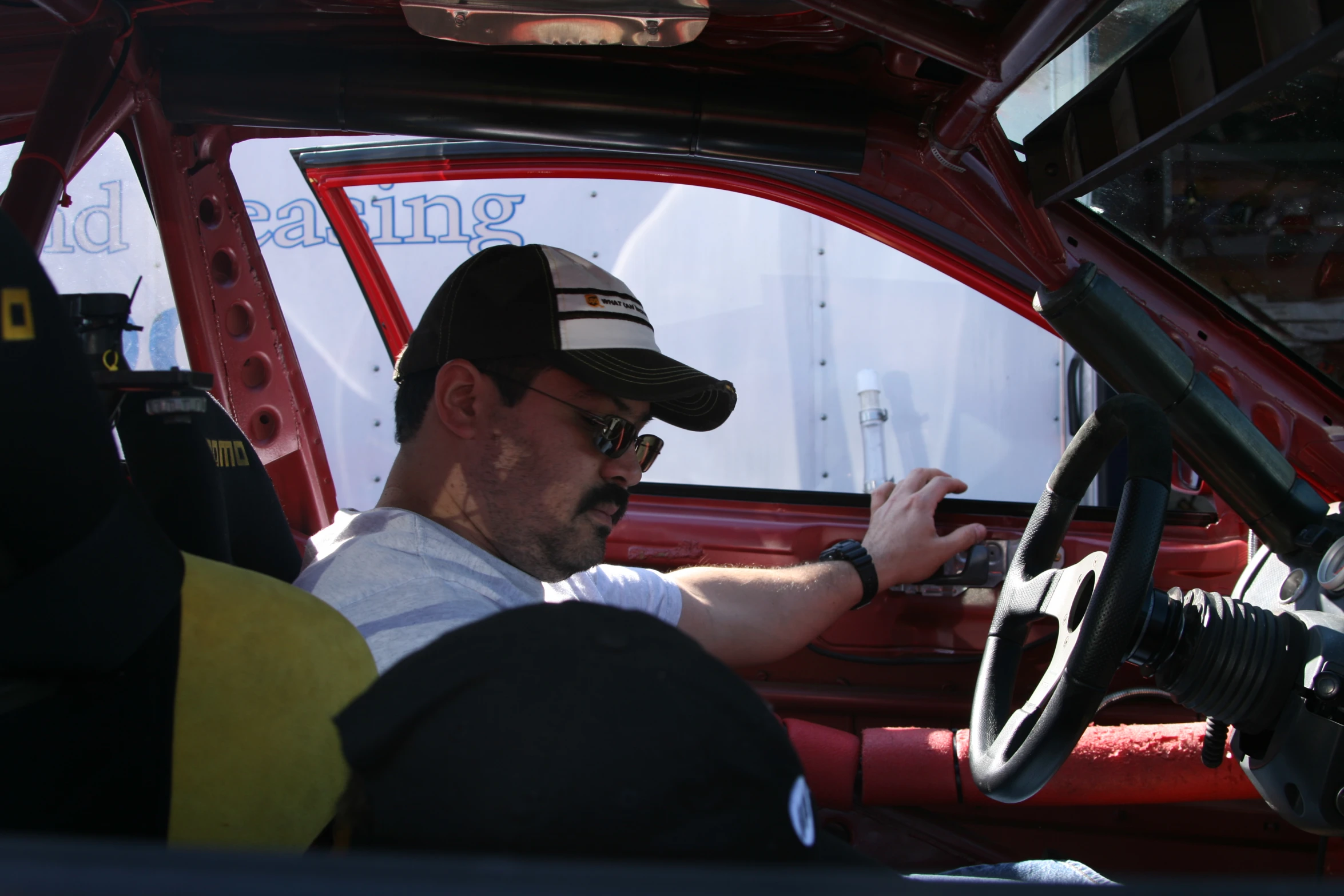 a man wearing sunglasses driving a truck with his hands on the steering wheel