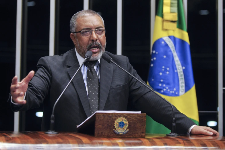 an older man speaking from behind a podium in front of flags