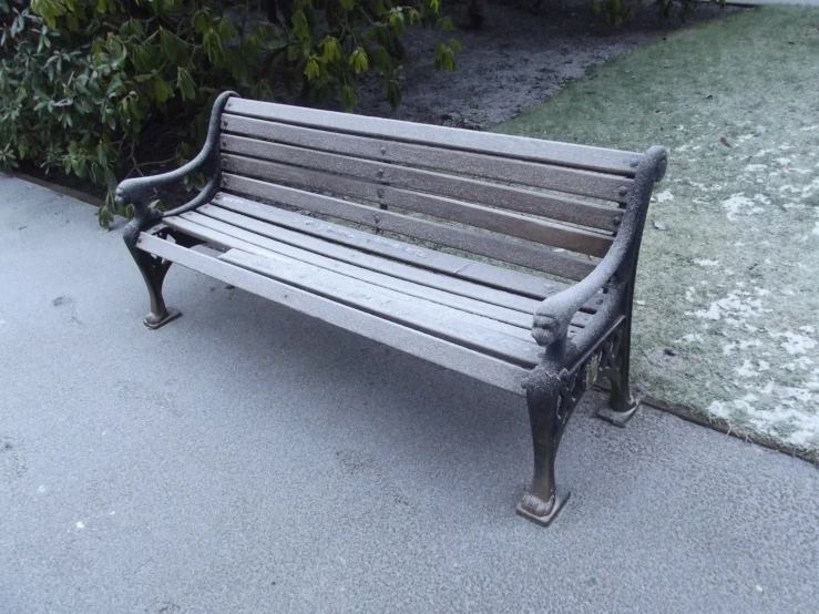 a wooden bench on the sidewalk next to some plants