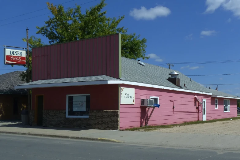 a small building with pink paint, a sign and large trees