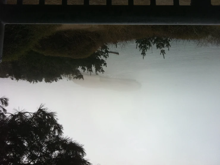 trees and fog are surrounding the reflection of a bridge in the water