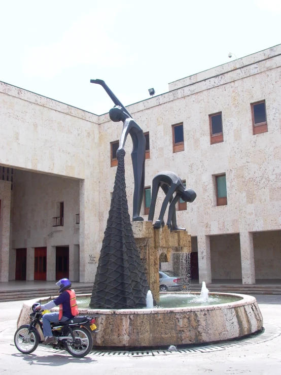 man riding on his motorcycle near a large artistic sculpture