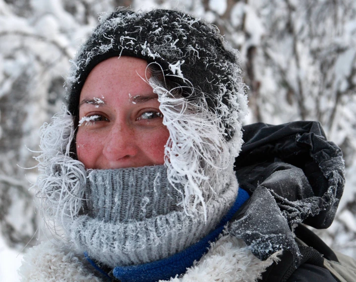 a woman with snow gear on her face and head in front of a snowy forest