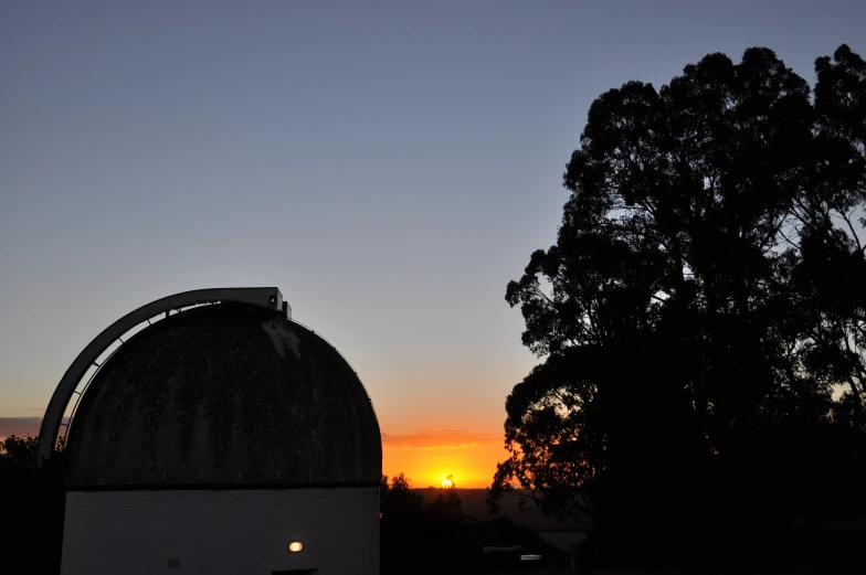 the sun is setting behind trees with a dome