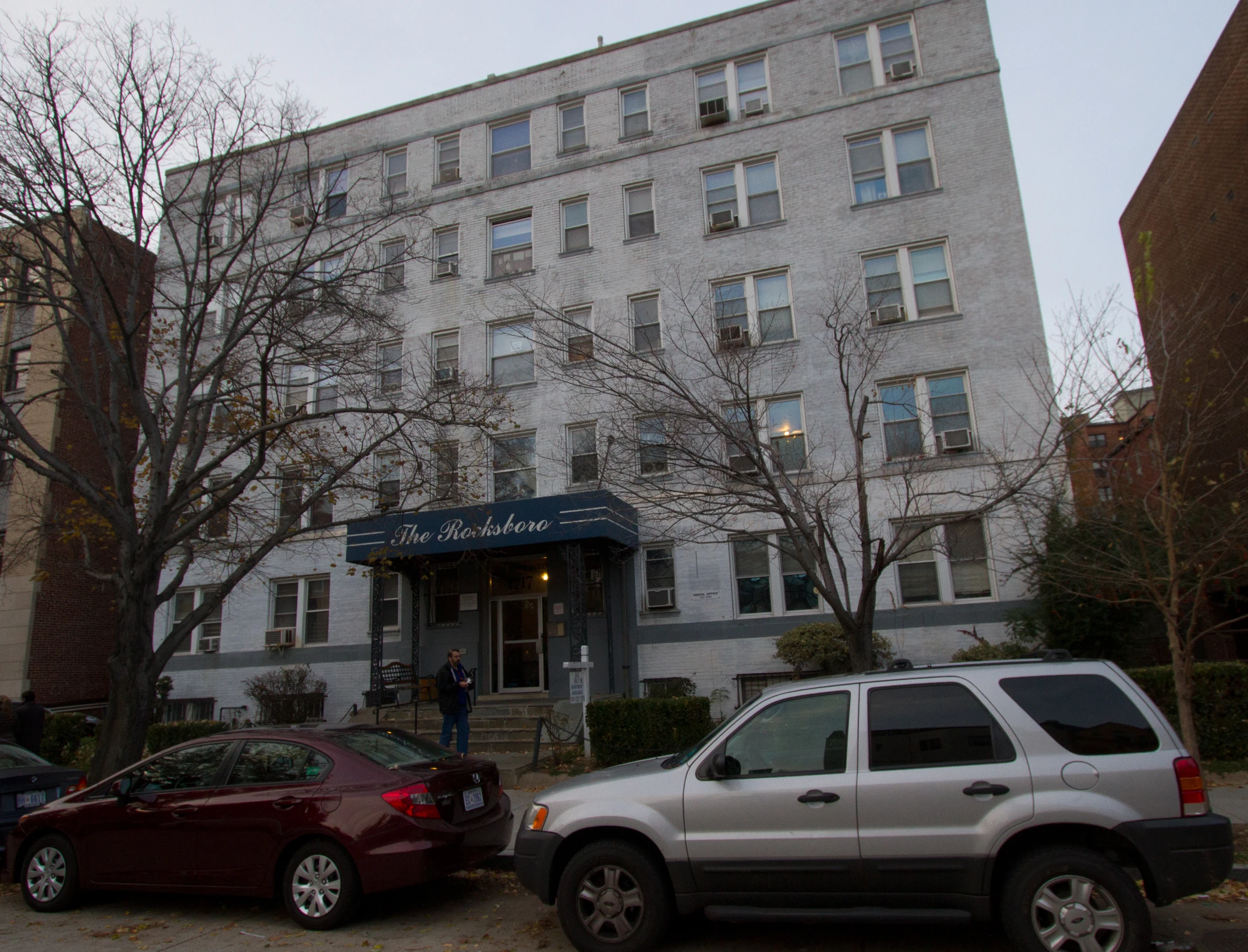 a man in the foreground and other cars near building