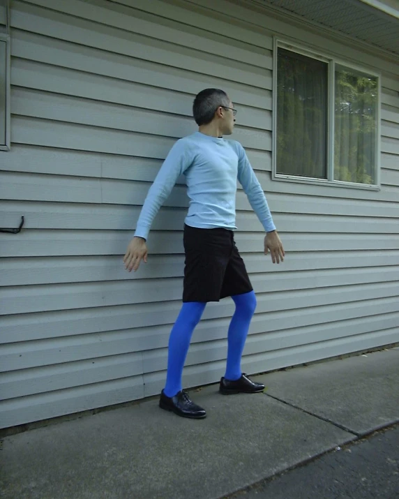 a man is leaning on the wall wearing a blue top and black shorts