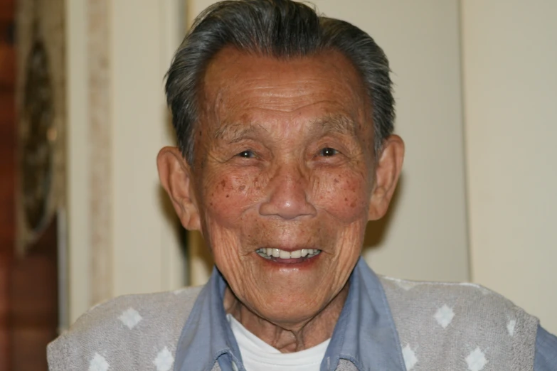 an elderly man smiling wearing a sweater over his sweater