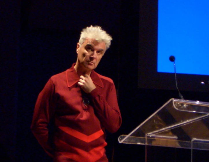 an elderly man talking on stage at a public event